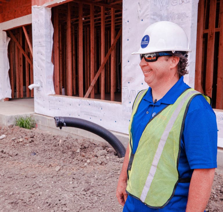 A Cardinal Strategies employee with a hard hat and reflective inspecting foundation drainage systems.