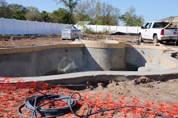 A residential swimming pool in the process of being built with bare concrete walls and steps and brown tile already set around the top edges.