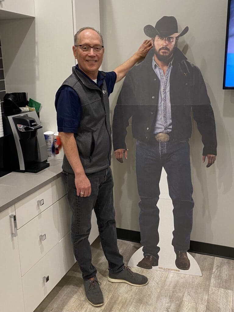 An employee of Cardinal Strategies standing in front of a cardboard figure.