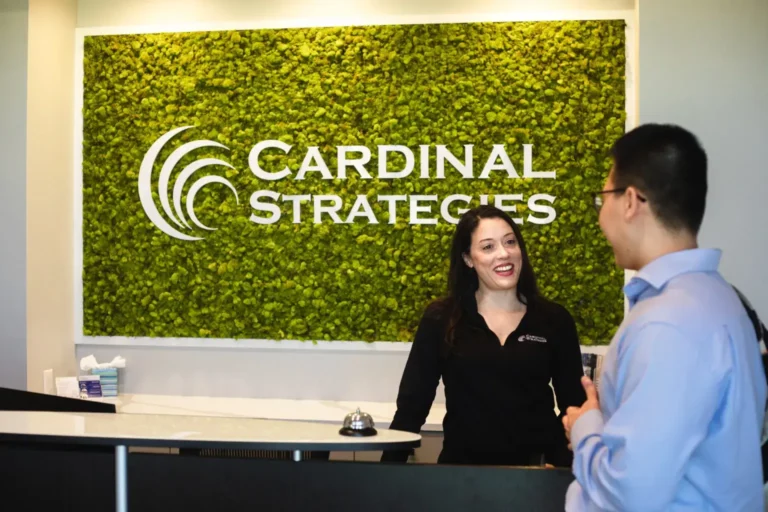 Brittany and Minh talking in lobby with Cardinal Strategies logo on wall in the background