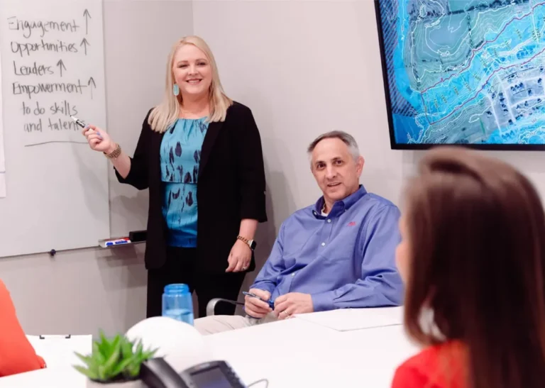 Kim pointing at whiteboard in conference room while talking with staff